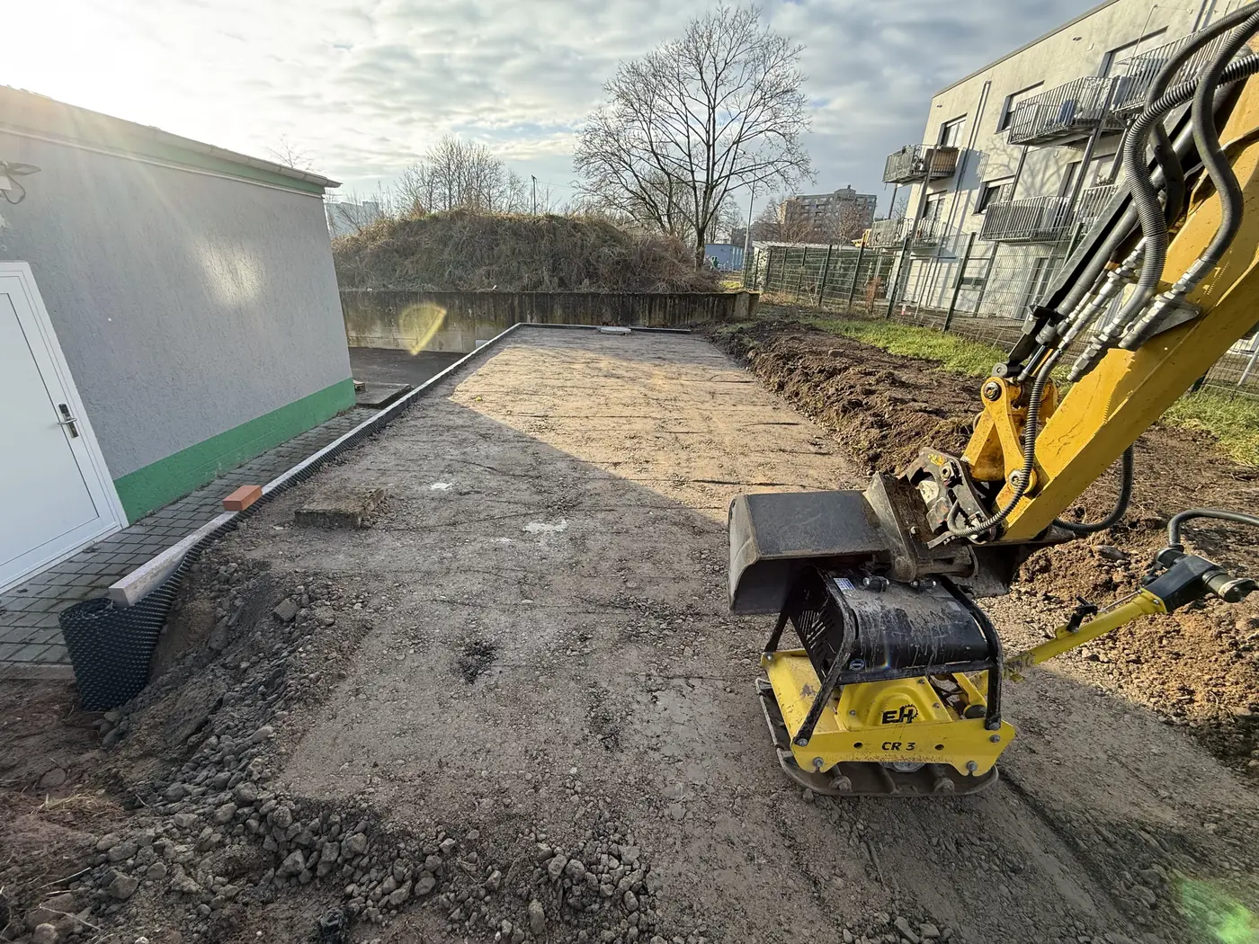 Bagger mit Anbau-Rüttelplatte verdichtet eine abgezogene Fläche